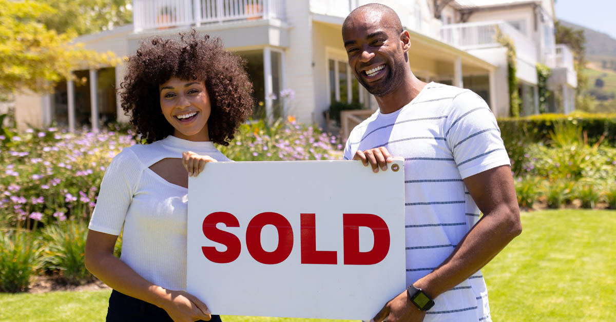 Couple with sold sign in front of home